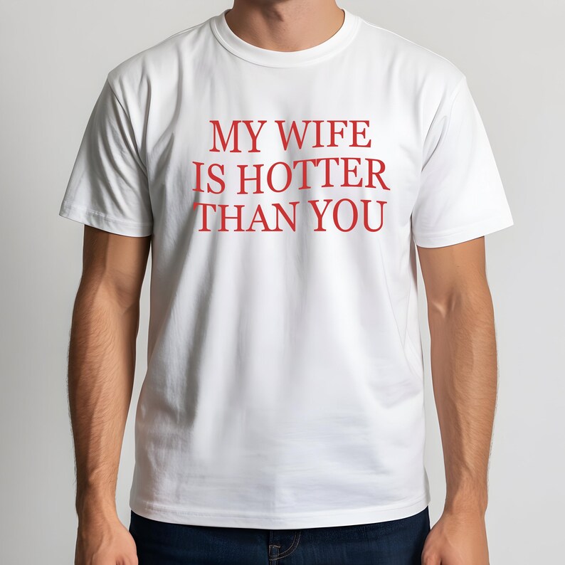 May include: White t-shirt with the red text "MY WIFE IS HOTTER THAN YOU". The shirt has short sleeves and a crew neck. The text is centered on the front of the shirt.