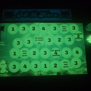 May include: A glow-in-the-dark board game featuring a path of numbered circles, text instructions like Roll and Save, Go Back to Start, and Go Back 2 Spaces, a shark illustration, a diver in a cage, and a six-sided die with black pips.