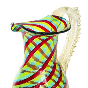 May include: A colorful glass pitcher with a ruffled rim and a decorative handle. The pitcher features a vibrant pattern of red, yellow, and blue stripes. The handle is a light beige color.