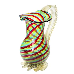 May include: A colorful glass pitcher with a ruffled rim and a decorative handle. The pitcher features a vibrant pattern of red, yellow, and blue stripes. The base and handle have a gold-colored finish. This decorative pitcher is ideal for serving beverages.