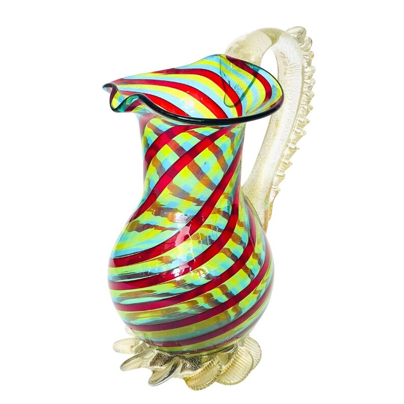 May include: A colorful glass pitcher with a ruffled rim and a decorative handle. The pitcher features a vibrant pattern of red, yellow, and blue stripes. The base and handle have a gold-colored finish. This decorative pitcher is ideal for serving beverages.