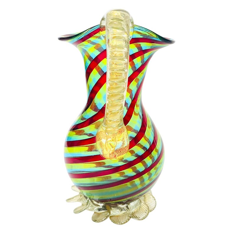 May include: A colorful glass pitcher with a gold handle and base. The pitcher features a vibrant design of red, yellow, blue, and green stripes. The handle and base have a gold finish, adding a touch of elegance to the decorative piece.