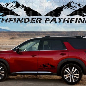 May include: A red Nissan Pathfinder SUV with black mountain decals on the doors. The decals feature the word "Pathfinder" in a stylised font. The vehicle is parked on a dirt road with a desert landscape in the background.