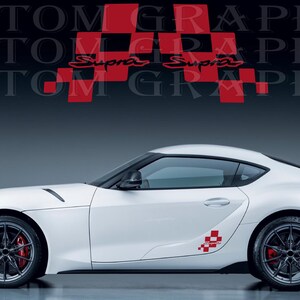 Puede incluir: Un coche deportivo blanco con llantas negras y pinzas de freno rojas. El coche tiene un diseño a cuadros rojos y blancos en el lateral y la palabra "Supra" en rojo. El fondo tiene las palabras "CUSTOM GRAPHICS" en un patrón repetido.