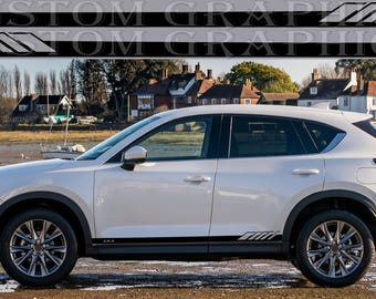 May include: A white Mazda CX-5 SUV with black side door decals. The decals feature a geometric pattern and the text "CX-5".