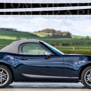May include: A dark blue convertible car with a black roof and black and silver side stripes. The car is labelled "MX-5" on the side.