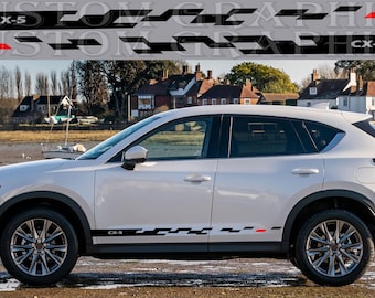 May include: White Mazda CX-5 SUV with black and red racing stripes decals. The decals feature a checkered pattern and the text "CX-5".