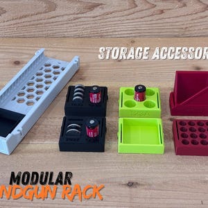 May include: A collection of modular storage accessories in various colors, including a white rack with a honeycomb design, black and green trays, and red containers. The text "STORAGE ACCESSORIES" and "MODULAR HANDGUN RACK" are visible.