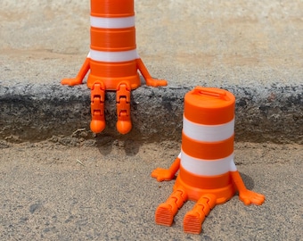 May include: Two orange and white traffic cone figurines with arms and legs are sitting on a concrete surface. The cones have a cylindrical shape with white stripes and a handle on top. The figurines are in a relaxed pose.