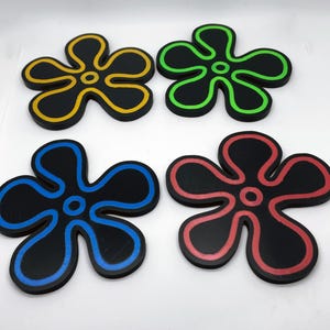 Puede incluir: Cuatro posavasos negros con forma de flor con contornos de diferentes colores. Los posavasos son amarillos, verdes, azules y rojos.
