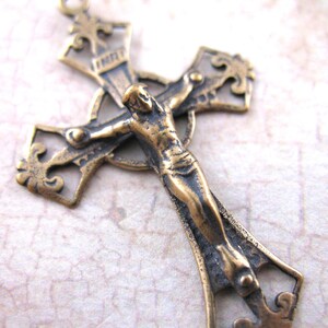 May include: A detailed bronze-colored crucifix with a figure of Jesus Christ. The cross has ornate, filigree-style detailing and a textured finish. The figure is in a traditional pose, with arms outstretched. The overall design is vintage and religious.