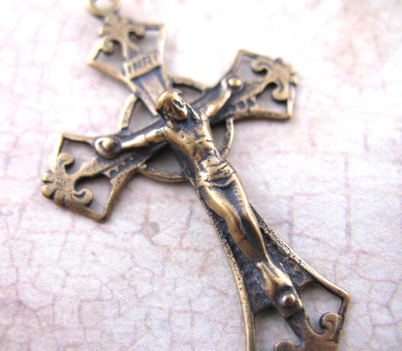 May include: A detailed bronze-colored crucifix with a figure of Jesus Christ. The cross has ornate, filigree-style detailing and a textured finish. The figure is in a traditional pose, with arms outstretched. The overall design is vintage and religious.