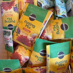 May include: A collection of yellow and green bags of Miracle-Gro Potting Mix, Seed Starting Potting Mix, and Tropical Potting Mix. The bags feature floral designs and the Miracle-Gro logo. The text "Twice As Big" is visible on some bags.