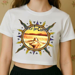 May include: White crop top featuring a circular graphic with the text "Alice in Chains" and an image of a person on a beach. The graphic is surrounded by a sunburst design with blue, yellow, and green accents.