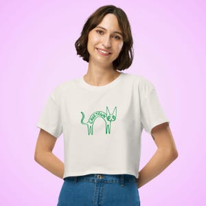 May include: Cream-colored crop top with a green cat graphic and the word "CAVETOWN" arched over the cat's back. The cat design is a simple, whimsical line drawing. The shirt has short sleeves and a crew neck.