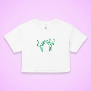 May include: White crop top with a green outline drawing of a cat. The word "CAVETOWN" is written in green inside the cat's body. The shirt has a crew neck and short sleeves.