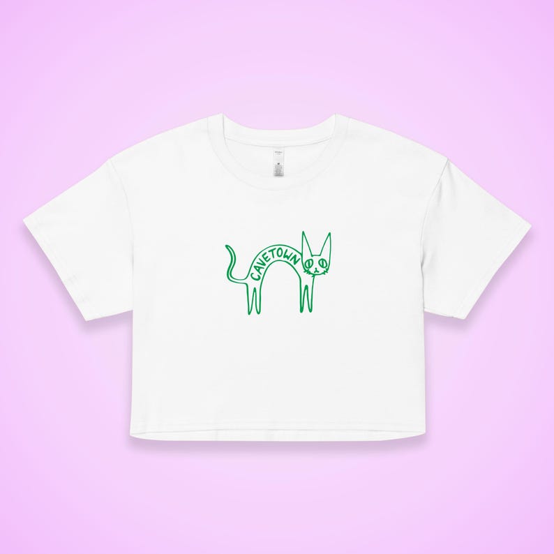 May include: White crop top with a green outline drawing of a cat. The word "CAVETOWN" is written in green inside the cat's body. The shirt has a crew neck and short sleeves.