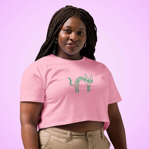 May include: A light pink crop top with a green outline of a cat and the word "CAVETOWN" in green. The shirt is made of a soft material and has short sleeves.