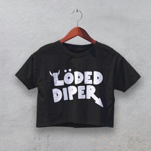 May include: Black crop top with the text "LÖDED DIPER" in white, featuring a devil horn above the "O" and an arrow pointing down. The shirt is hanging on a wooden hanger against a gray background.