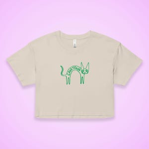 May include: A beige crop top with a green outline drawing of a cat. The word "CAVETOWN" is arched over the cat's back. The cat has a long tail and is standing on its hind legs. The shirt has short sleeves and a crew neck.