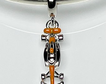 May include: A silver charm in the shape of a Formula 1 race car with orange and black accents. The charm is suspended from a silver loop, and is designed to be added to a bracelet or necklace.