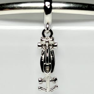 May include: A silver-toned metal charm shaped like a Formula One race car, featuring a streamlined body, four small wheels, and a top-mounted loop for attachment. The charm is suspended from a polished silver-toned horizontal metal bar.