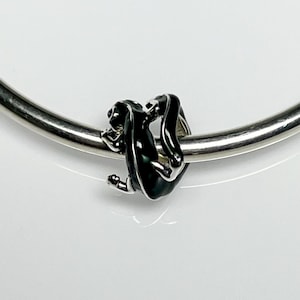 May include: A black and silver charm featuring a monkey design. The monkey is black with silver accents, hanging from a silver bracelet. The charm is detailed and has a glossy finish, suitable for jewelry.