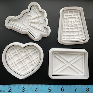 May include: Set of four white plastic cookie cutters shaped like a bagpipe, a kilt, a heart with a plaid pattern, and a Scottish flag.