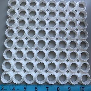May include: A white plastic grid of scalloped-edge cookie cutters. The cutters are arranged in a matrix. A ruler shows measurements in inches, equivalent to approximately 7.6 to 25.4 cm.