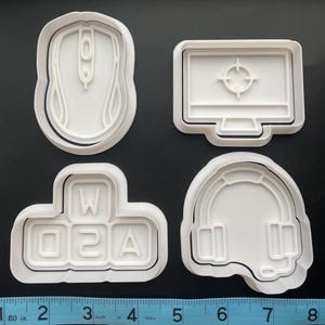 May include: Set of four white plastic cookie cutters shaped like a computer mouse, a computer monitor with a target in the center, a keyboard with the letters W, Q, 2, and A, and a headset with a microphone.