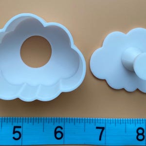 May include: White plastic cookie cutters shaped like clouds. The larger cutter has a hole in the center. The smaller cutter has a handle on the back.