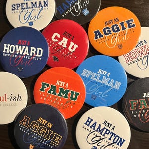 May include: A selection of circular badges displaying university names and the words "Just a Girl" in cursive. The badges are in shades of blue, orange, red, and black, with text in white and other colours. They are arranged on a dark surface.