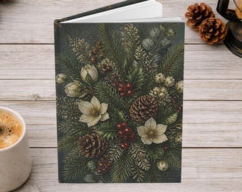 May include: A hardcover journal featuring a dark green cover with a detailed botanical illustration of pine branches, brown pinecones, red berries, and white hellebore flowers. The book is slightly open, revealing white pages inside.