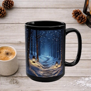 May include: A black ceramic mug featuring a printed illustration of a snow-covered path winding through a dark blue forest at night. Two glowing lanterns illuminate the snowy steps, while small white lights are scattered among the trees.