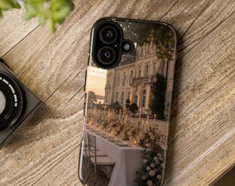 May include: A smartphone case featuring a printed image of an outdoor dining setup at dusk, with a long table covered in a white cloth, floral centerpieces, and lit candles in front of a large stone building with architectural details.
