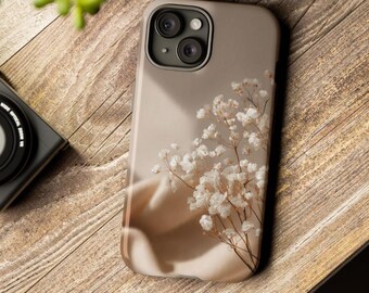 May include: A beige smartphone case featuring a printed design of delicate white baby's breath flowers. The case has a cutout for a dual-lens camera system and a smooth, matte finish, showcasing a soft, neutral color palette throughout.