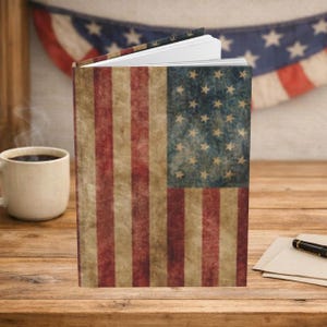 May include: A hardcover journal featuring a weathered, vintage-style American flag design on the front cover. The cover displays the classic red, white, and blue stripes with a blue field of white stars, all presented with a distressed, aged texture.