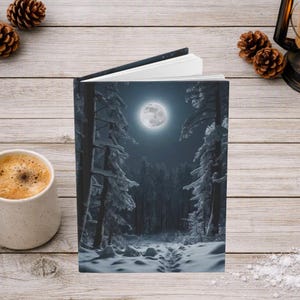 May include: A hardcover book featuring a nighttime winter forest scene on the cover, depicting snow-covered pine trees, a path leading into the woods, and a bright full moon in the dark sky. The book is open slightly, showing white pages.