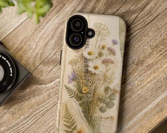 May include: A phone case featuring a collage of pressed dried flowers, including white daisies, lavender, and green ferns, set against a cream-colored background with a textured paper effect and a black camera lens cutout.