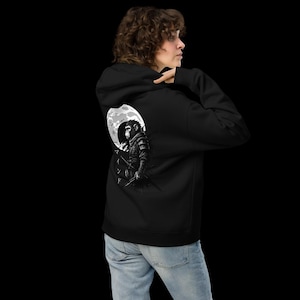Könnte beinhalten: Schwarzer Kapuzenpullover mit einer schwarz-weißen Grafik eines Samurai-Affen auf dem Rücken, vor einem Vollmond. Die Person, die den Hoodie trägt, trägt auch eine blaue Jeans. Das Design ist in Schwarz und Weiß gehalten.
