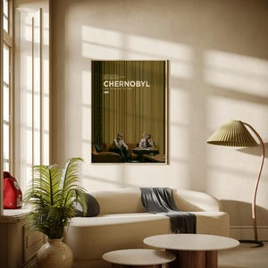 May include: A framed rectangular poster for the television series Chernobyl, featuring a dark olive green background with vertical lines, the title text in white, and an image of two people sitting on a sofa, displayed on a light beige wall.