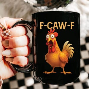 May include: Black ceramic mug with a cartoon chicken illustration. The chicken is orange and yellow with a red comb and wattle, and the mug has the text "F-CAW-F" in yellow.