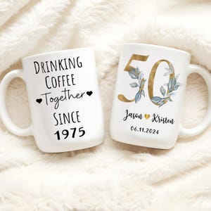 Two white ceramic mugs with text and designs on them.