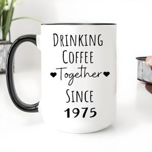 A white coffee mug with black text that reads "Drinking Coffee Together Since 1975".