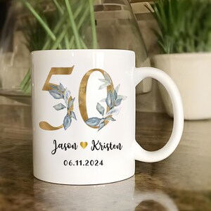 A white ceramic mug with a gold and blue floral design, featuring the number 50 and the names 'JASON' and 'KRISTEN' printed on it.