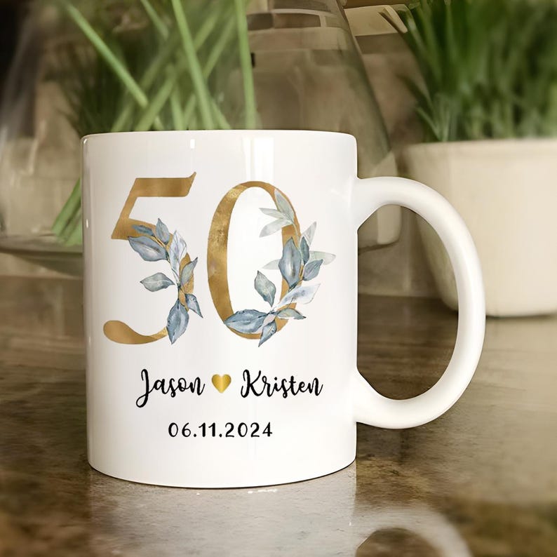 A white ceramic mug with a gold and blue floral design, featuring the number 50 and the names 'JASON' and 'KRISTEN' printed on it.