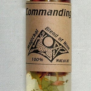 May include: A small glass bottle with a black cap filled with a clear liquid and dried herbs. The label reads "Commanding Magickal Blend of Nine 100% Natural".