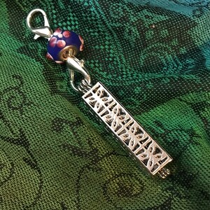 May include: Silver charm with a blue and white glass bead and a decorative filigree design.
