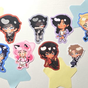 May include: A collection of eight die-cut stickers featuring chibi-style anime characters with diverse hair colors, outfits, and expressions, arranged alongside several pastel-colored star-shaped paper cutouts on a plain white surface.