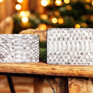 May include: A rectangular card holder and a bifold wallet, both featuring a textured white and grey snakeskin pattern with visible stitching along the edges. The items are positioned side by side, displaying their exterior surfaces clearly.